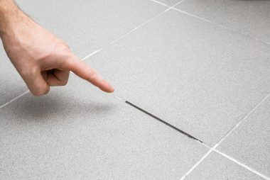 mans-hand-finger-pointing-to-space-between-tiles-damaged-tiles-seam-building-problem-concept